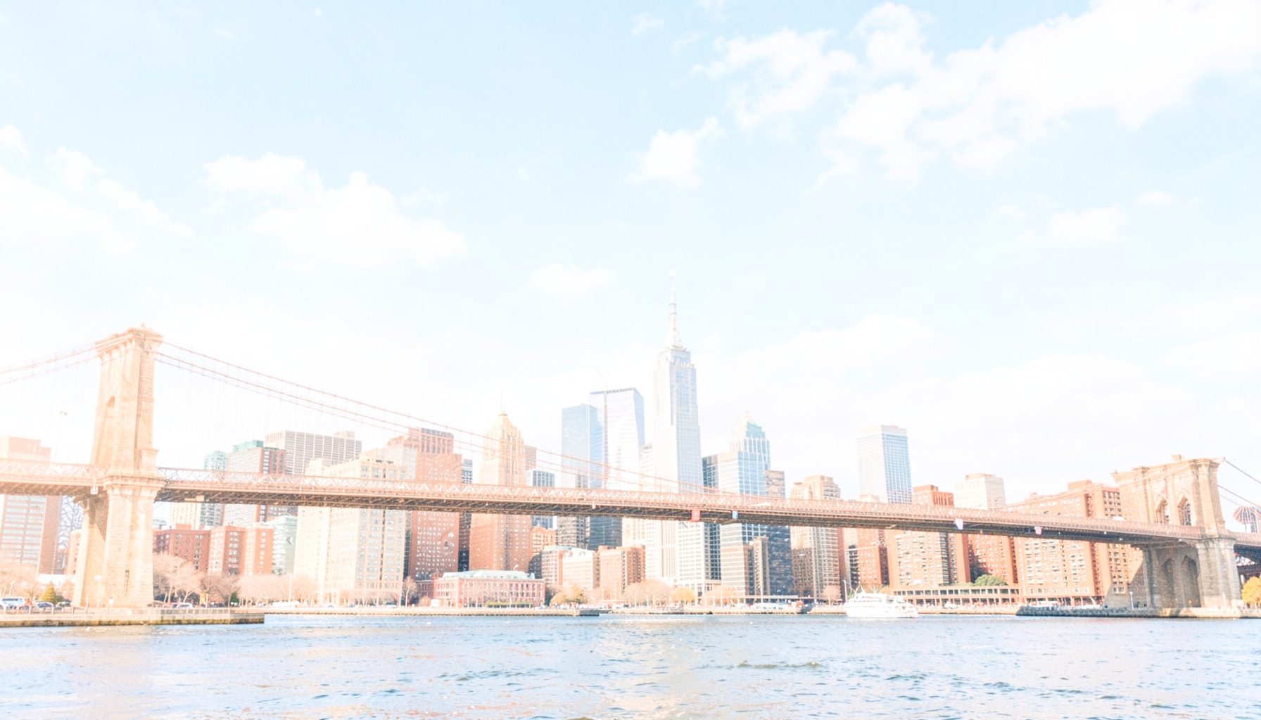 Bright, airy photograph of a New York City skyline view with blue skies and soft clouds over the Manhattan bridge area