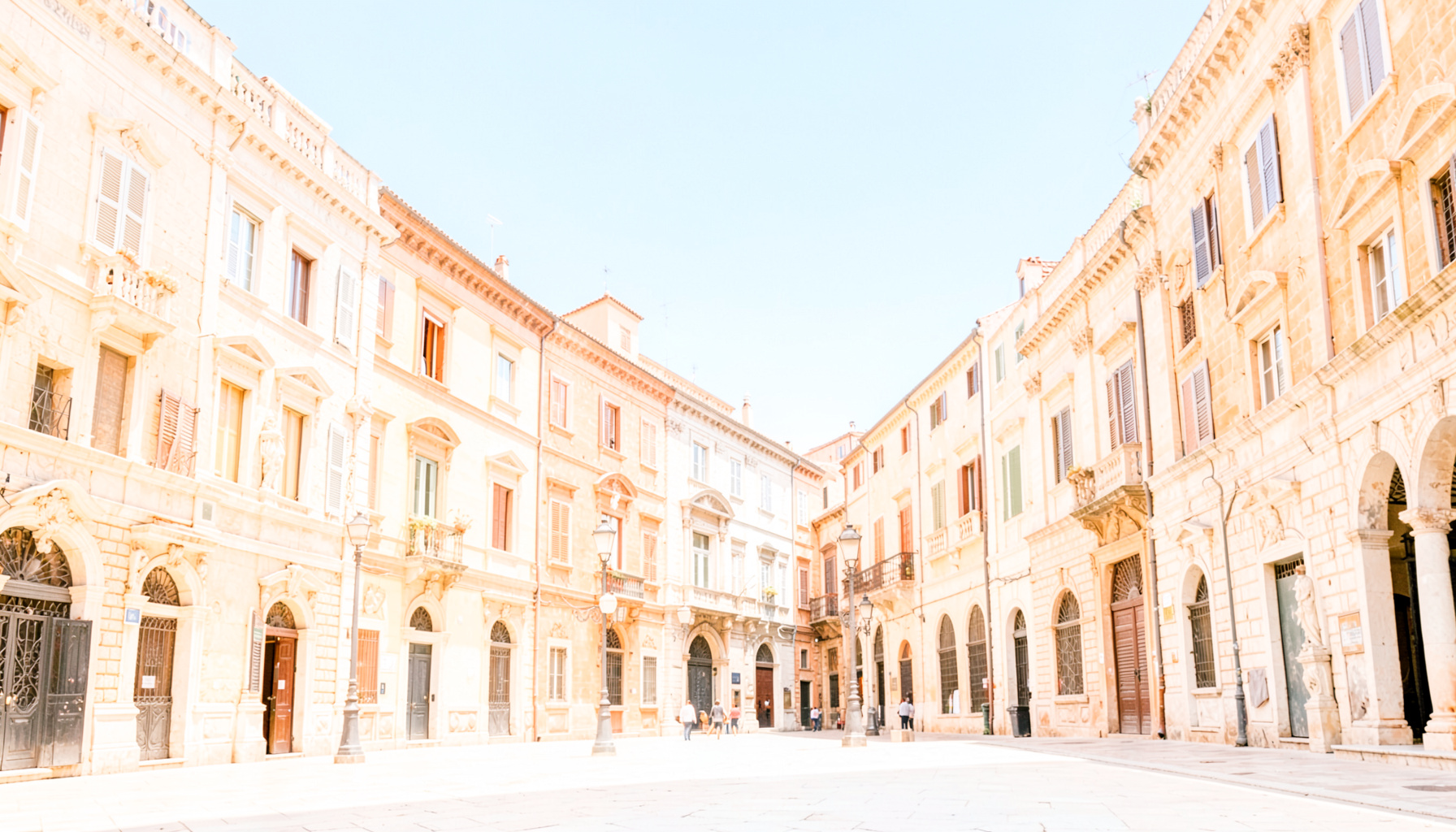 Bright, airy photograph of a sunlit European piazza with historic stone architecture and a clear blue sky